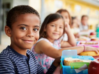 Young boy and girl at school lunch table smiling to camera