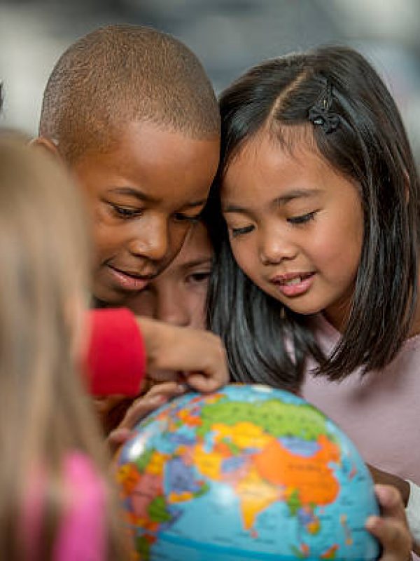 A multi-ethnic group of elementary age students are learning the places of the world by looking at a globe in geography and history class.