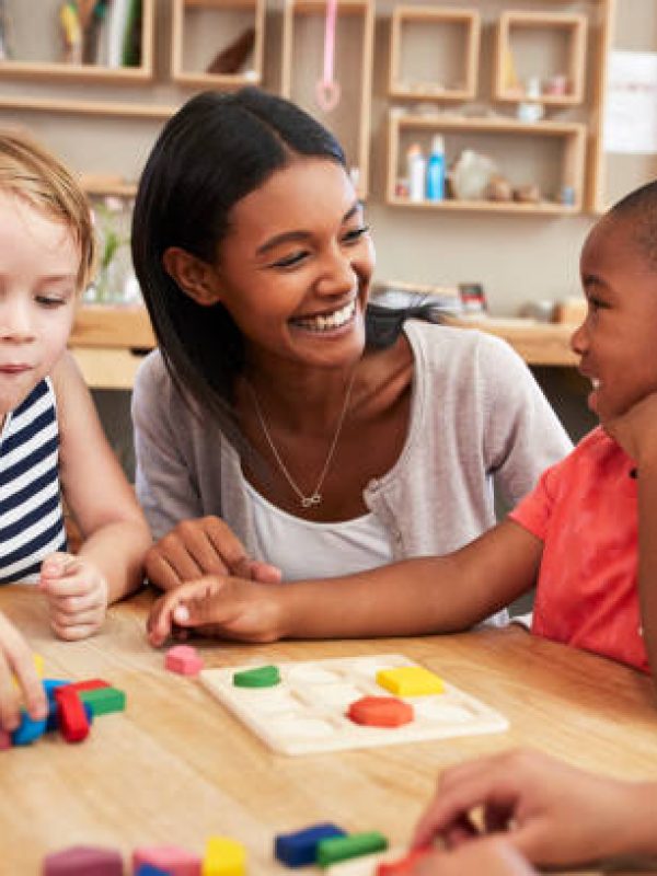 Teacher And Pupils Using Wooden Shapes In Montessori School